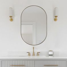 a bathroom vanity with two sinks and a large round mirror above it, along with gold faucets