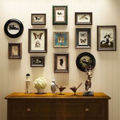 there are many framed pictures on the wall above a dresser with vases and flowers