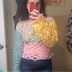 a woman taking a selfie in front of a mirror with her cell phone and wearing a crocheted sweater