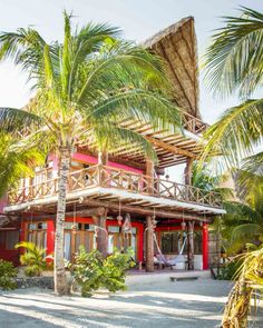 a red house surrounded by palm trees on the beach with a hammock hanging from it's roof