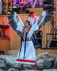 a woman dressed in native american clothing holding her arms out with wings outstretched while performing on stage