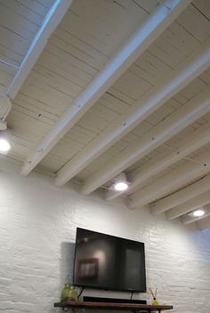 a flat screen tv mounted to the side of a white brick wall in an empty room