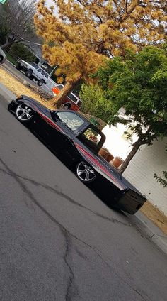 a black and red car parked on the side of a road next to a tree