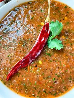 a red chili pepper is in a white bowl with some cilantro on the side