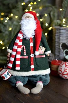 a santa clause doll sitting on top of a table next to a christmas tree and presents