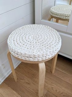 a white wicker stool sitting on top of a wooden floor next to a mirror