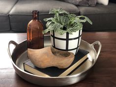 a metal tray with a wooden shoe, bottle and plant in it on a table