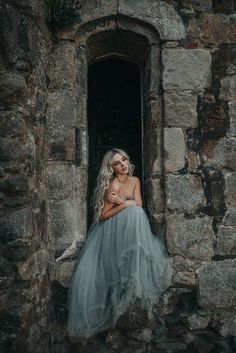 a woman in a blue dress is sitting on a stone wall and looking out the window