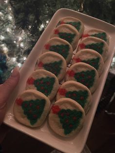 a white plate topped with cookies covered in frosting next to a green and red christmas tree