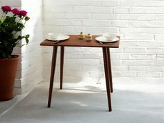 a small table with two plates on it next to a potted plant and brick wall