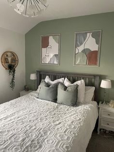 a bedroom with green walls, white bedding and two framed pictures on the wall