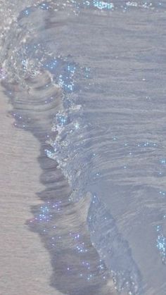 a person walking on the beach with their surfboard in hand and sparkling water behind them