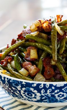 a blue and white bowl filled with green beans, potatoes and bacon on a table