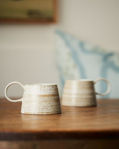 two white cups sitting on top of a wooden table next to a blue chair in the background