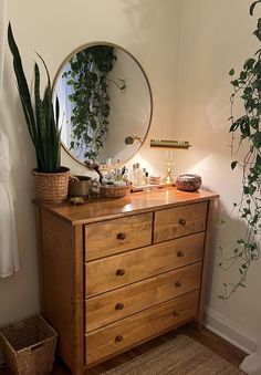 a wooden dresser topped with a mirror next to a potted plant and wicker basket