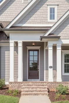 a gray house with white trim and brick steps leading up to the front door that is flanked by two windows