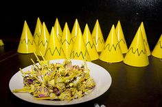 there is a plate with candy in it and many yellow cones on the table behind it