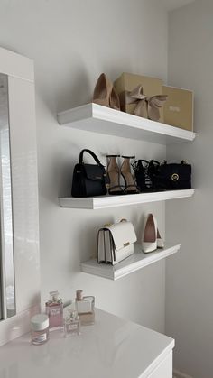 two white shelves filled with purses and handbags on top of each other next to a mirror