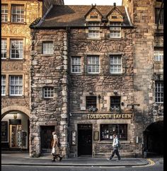 two people walking past an old stone building