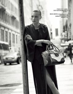 a woman is leaning against a pole with her handbag on it's shoulder