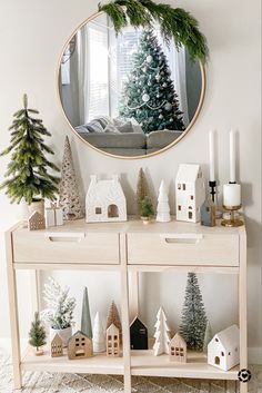 a christmas scene with miniature houses and trees on a shelf in front of a mirror