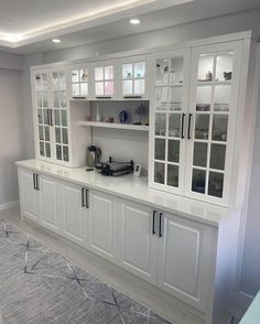 a kitchen with white cupboards and glass doors on the front, along with an area rug