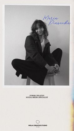 a woman sitting on top of a stool in front of a white wall with blue writing