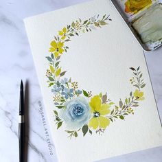 a watercolor painting of yellow and blue flowers on white paper next to a brush