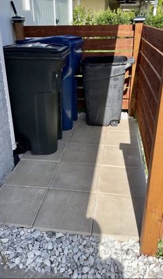 two trash cans sitting next to each other on top of a cement floor in front of a wooden fence