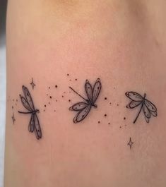 three small dragonflies on the back of a woman's thigh, with stars around them