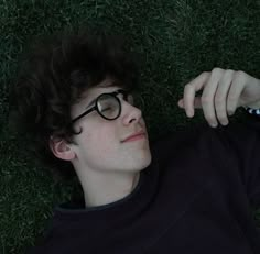 a young man laying in the grass with glasses on