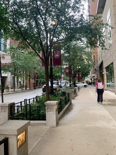 a woman walking down a sidewalk in front of a tall building with trees on both sides