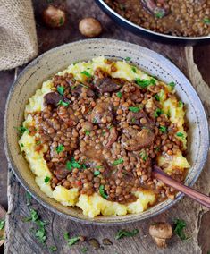 a bowl filled with mashed potatoes covered in sausage and lentils on top of a wooden table