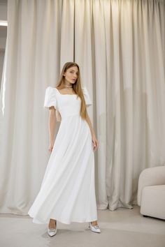 a woman standing in front of a curtain wearing a white dress with ruffle sleeves