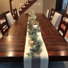 the table is set for dinner with candles and greenery on it, along with other decorations