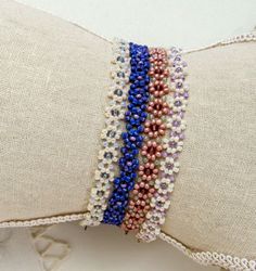 three bracelets on top of each other in different colors and sizes, sitting on a pillow