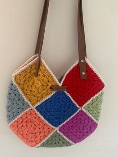 a multicolored crocheted bag hanging on a wall with brown leather handles