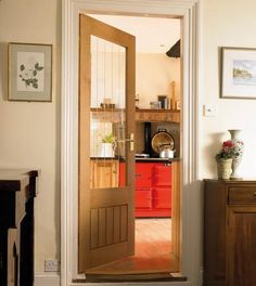 an open door leading to a kitchen and living room with red furniture in the background