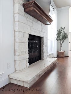 a living room with a white brick fireplace and wood flooring, along with a potted plant