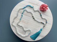 "Ukiyo 108 Bead Mala Necklace \"Ukiyo\" meaning the floating world, to live in the moment, separated from the worries of life. White Jade Blue & White Flower Jade Length- 22\" Bead Size- 6mm Thread- Muted Blue Silk Tassel- Blue Rayon Accents/Charm- Silver metal alloy  A note from the seller, K. Creative Intuition Every Mala, Every Soul Unique. Creative Intuition is the ability to realize useful creative ideas without thought. Each mala is made with this intention. If we can achieve the fluid sta Adjustable Crystal Necklaces With 8mm Beads For Gifts, Adjustable Spiritual Beaded Necklaces For Gifts, Spiritual Round Bead Crystal Necklaces For Beach, Adjustable 8mm Bead Necklaces For Beach, Spiritual Beaded Necklaces For Beach, Spiritual Crystal Necklaces With Round Beads For Beach, Adjustable 8mm Beaded Necklace Gift, Spiritual Beaded Necklaces For Meditation With Faceted Beads, Turquoise Beaded Crystal Necklaces For Meditation