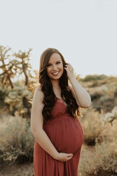 a pregnant woman in an orange dress smiles at the camera while posing for a photo