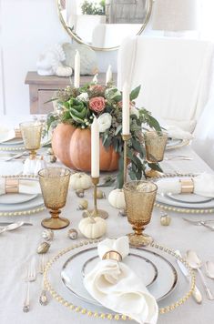 a dining table set for thanksgiving dinner with candles, plates and flowers in the center