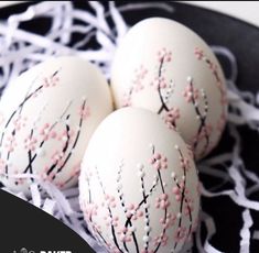 three white decorated eggs sitting on top of a black plate with pink and white sprinkles