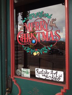 a merry christmas sign is in the window of a store front with green and red trim