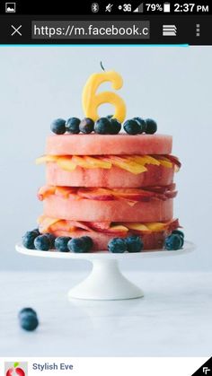 a birthday cake with blueberries and oranges on it is sitting on a white pedestal