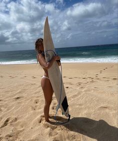 a woman holding a surfboard on top of a sandy beach next to the ocean