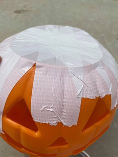 an orange and white plastic pumpkin sitting on top of a cement ground