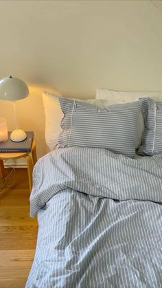 a bed with blue and white striped comforter next to a lamp on a nightstand