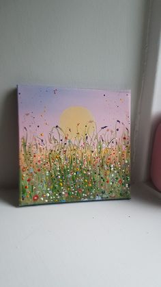 a painting on a white surface next to a pink box with a yellow sun in the background