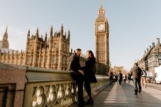 two people standing next to each other in front of big ben and the palace of westminster